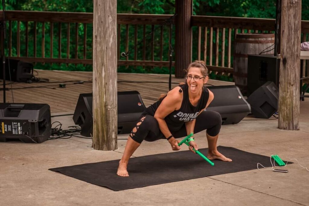 Rocking Wellness: An Interview with Jannette Parent 4 Jannette Parent, a Kentucky Yoga Festival instructor, is teaching POUND. She is in a squat on top off a black yoga mat holding drum sticks. Her tongue is sticking out in a "rock out" style of dance.